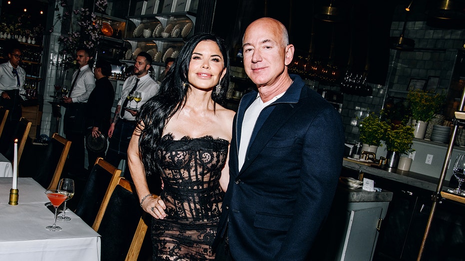 Lauren Sanchez wearing a lace black dress and Jeff Bezos wearing a navy colored suit