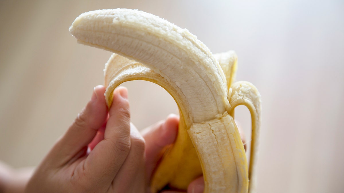 A hand unpeels a banana.